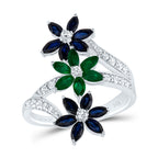 White gold diamond ring with three stacked flower designs, featuring two blue sapphire flowers on the sides and one emerald flower in the center.
