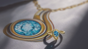 Aquamarine gold ring laying on paper with a drawing of the ring, featuring text: 'Custom jewelry from concept to creation, contact us.'