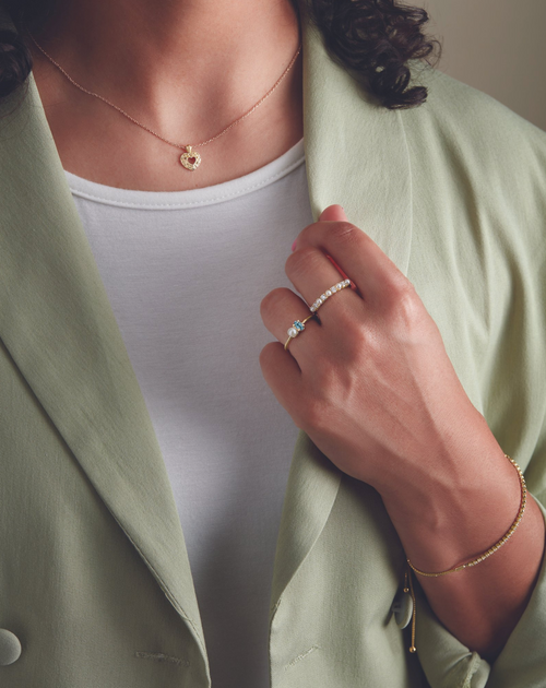 A woman wearing a white shirt and green blazer, modeling a diamond ring and bracelet on her arm.