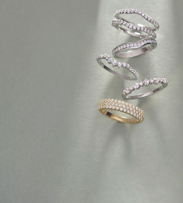Three diamond rings stacked: bottom is white gold, middle is rose gold, and top is white gold, each with five stones, displayed on a grey background.