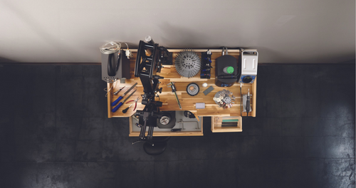 Top view of a jewelry workbench with repair tools on a wood-colored surface, set against a black and white background