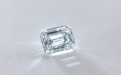 A single emerald-cut diamond on its side, displayed on a light grey background.