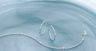 A woman's hand and arm wearing diamond and gold bracelets, dressed in a navy blue shirt, displayed on a blue background