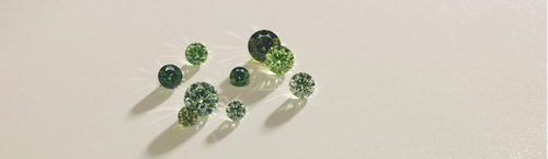 Multiple loose green stones in different shades, displayed on a tan background.