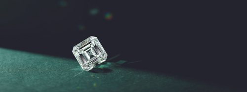 A single square stone tilted on its side, with a diamond reflection, set against a dark teal background.