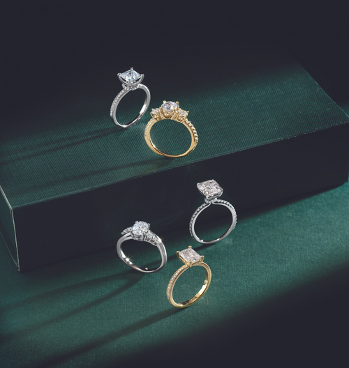 Three white gold solitaire rings and two yellow gold solitaire rings, staggered on a dark green surface