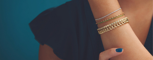 A woman's hand and arm wearing diamond and gold bracelets, dressed in a navy blue shirt, displayed on a blue background 