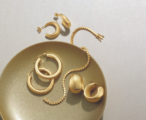 Loose gold jewelry: three pairs of gold hoops and a gold bracelet, displayed on a gold plate with a white background