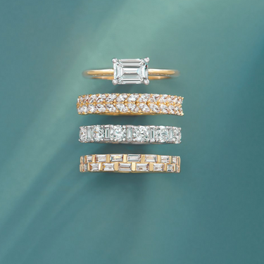 White and yellow gold diamond bands leaning against each other on a white background with a white cloth to the left hand side