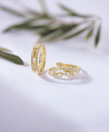 Three diamond bands: one tilted, two leaning on each other, against a white background with blurred green leaves in the distance
