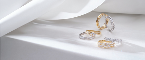 White and yellow gold diamond bands leaning against each other on a white background with a white cloth to the left hand side