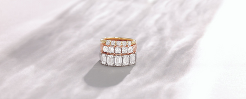 Three diamond rings stacked: bottom is white gold, middle is rose gold, and top is white gold, each with five stones, displayed on a grey background.