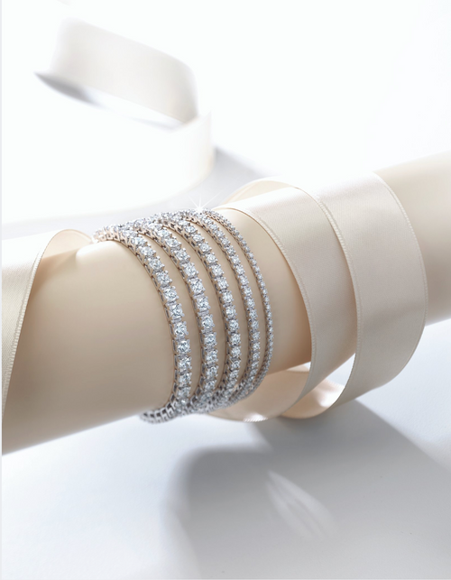 Five white gold diamond bracelets on a tan display with a satin ribbon, set against a white background.